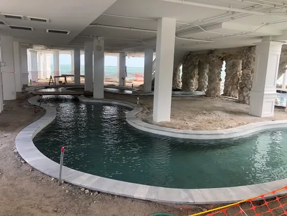 Ground-level lazy river and grotto pool under construction on Key Haven, with rock columns and open-water views